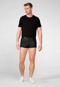 Zwarte katoenen T-shirt gecombineerd met aansluitende zwarte leren shorts met voorzakken en een ritssluiting, aangevuld met witte sneakers.