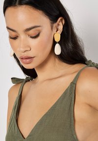 Yellow and cream drop earrings with an irregular shape. The top is a smooth, rounded yellow piece, and the bottom is a glossy cream teardrop.
