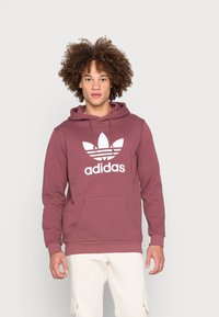 Raudonas gobtuvas su sweatshiru, pagamintas iš medvilnės mišinio, su dideliu baltu Adidas logotipu per krūtin�ę. Įeina priekinė kišenė ir raišteliai gobtuvui.