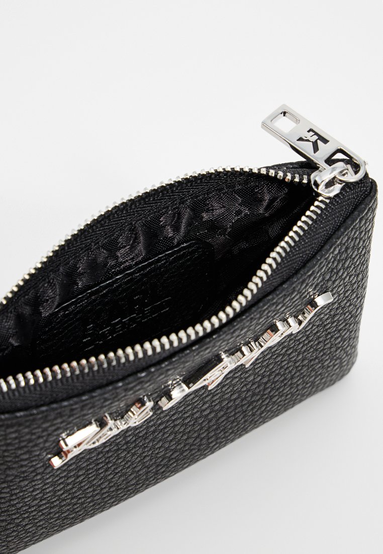 Cartera de cuero negro texturizado con un cierre de plata y acento de logo, que cuenta con un forro interior con diseño y forma rectangular compacta.