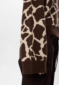 Pull en maille brun avec un motif de girafe beige, à coupe décontractée et manches longues, tissu texturé et poignets côtelés.