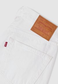 Jeans de mezclilla blanca mostrando el bolsillo trasero, la etiqueta roja de Levi's y el parche de cuero marrón de la marca Levi Strauss & Co. en la cintura.