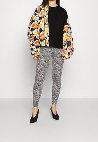 Giacca bomber floreale nera, arancione e gialla; maglietta nera; leggings a fantasia bianco e nero; scarpe con tacco nere.