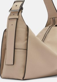 Sac en cuir beige à bandoulière avec une forme triangulaire unique, une surface texturée et une bordure noire. Il dispose d'une sangle ajustable et de quincaillerie en métal.