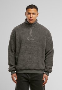 Fleece half-zip genser i mørkegrå med teksturert overflate, ribbede mansjetter og kant, med en minimalistisk brodert logo på brystet.