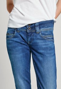 Blå denimjeans med standard passform, framfickor och dubbelknäppning. Tyget har en slät struktur med lätt blekning.