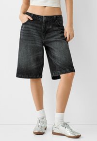 Black denim shorts with a relaxed fit, rolled hem, and five-pocket design, paired with metallic sneakers and white crew socks.