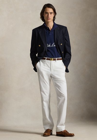 Tengerészkék blézer arany gombokkal, kék póló fehér felirattal, fehér nadrág és barna mokaszinek. Simogató textúrák és klasszikus, testre szabott szabás.