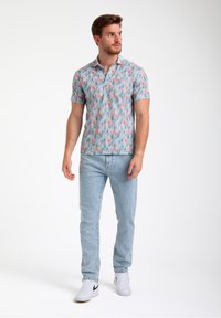 Camisa polo de manga corta, de color azul claro, con un patrón colorido de ciervos y árboles, combinada con jeans azul claro y zapatillas blancas.