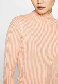 Maglione a maniche lunghe, aderente, in pesca chiaro con texture a coste verticali. Tessuto morbido con un leggero lucido. Collo alto e silhouette slim.