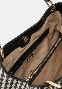 Borsa intrecciata in bianco e nero con hardware dorato, un ampio interno che presenta una tasca con zip e una fodera beige con motivo ripetuto "GUESS".