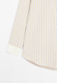 Striped shirt in light beige and pastel colors, featuring a white cuff and button closure, with a curved hem and smooth texture.