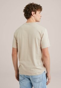 Béžové bavlněné tričko s krátkým rukávem, kulatým výstřihem a hladkou strukturou, nošené s světle modrými džíny.