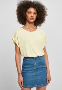 Lys gul kortærmet skjorte med en løs pasform, parret med en tætsiddende blå denim mini nederdel. Simpelt design med minimal detaljering.