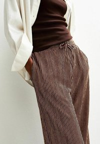 Pantalons rayés marron et crème avec une coupe décontractée, taille avec cordon de serrage et poches latérales, associés à un débardeur ajusté marron et une chemise blanche.
