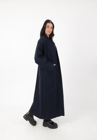 Largo abrigo azul marino hecho de mezcla de lana, con un silueta relajada, bolsillos laterales y mangas anchas, combinado con zapatos de plataforma negros.