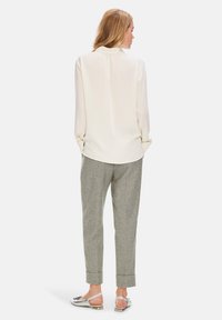 Helle Creme-Bluse mit Knopfrücken und langen Ärmeln, kombiniert mit grauen karierten, taillierten Hosen und silbernen flachen Sandalen.