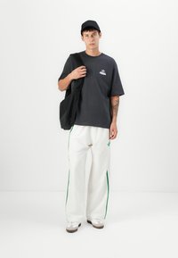 Sort bomulds T-shirt med lilla logo, hvide bukser med grønne striber, sort kasket og en sort tote bag. Brune og hvide sko.