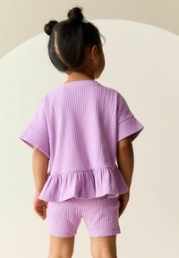 Fioletowy prążkowany t-shirt z baskinką, w komplecie z pasującymi fioletowymi szortami z kwiatowym wzorem. Teksturowana tkanina, luźny krój.