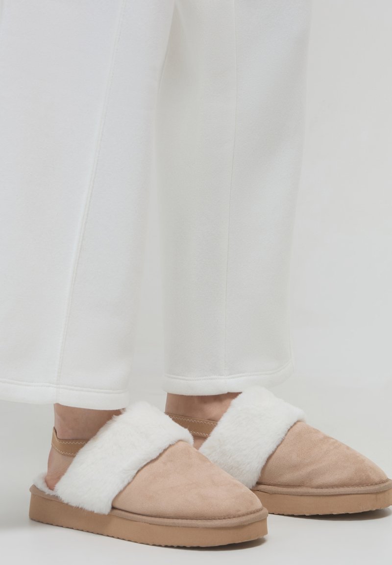 Pantofole aperte in suede beige, con una fascia in pelliccia sintetica bianca e una suola lavorata. Le pantofole presentano una finitura morbida e una punta rotonda.