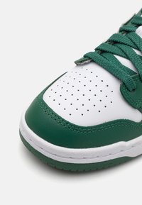 Sneaker verde e bianco con tomaia in pelle testurizzata, punta perforata, lacci verdi e suola bianca con un accento verde.