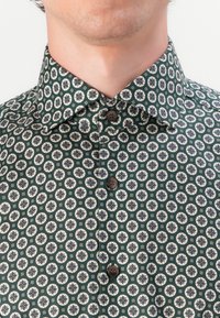 Grünes gemustertes Hemd mit einem geometrischen Design, aus einem Stoff mit glatter Textur gefertigt und mit Knopfverschlüssen auf der Vorderseite.