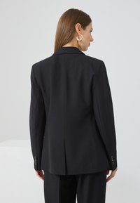 Černý saka s přizpůsobeným střihem, strukturovaným tvarem, klopovým límcem a knoflíkovými manžetami. Hladká látka, klasický design a čistý zadní pohled.