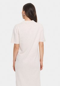 Ljus beige polo klänning med korta ärmar, mjukt bomullsmaterial, avslappnad passform och en detalj vid kragen bak. Minimalistisk design, slät textur.