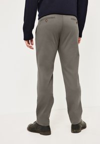 Graue Hose aus Stoff mit glatter Textur, ausgestattet mit Gesäßtaschen und braunen Knopfdetails. Kombination mit schwarzen Schuhen.