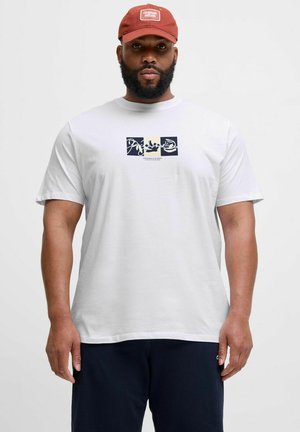 Weißes Baumwoll-T-Shirt mit einem zentralen Grafikdesign in Blau und Beige. Kurze Ärmel und lockere Passform. Getragen mit einer roten Mütze.