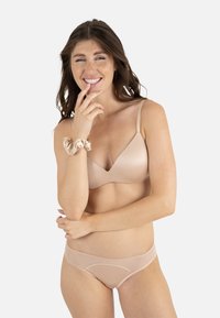 Soutien-gorge couleur nude en tissu lisse avec bretelles réglables, assorti à un slip translucide assorti présentant un détail de couture subtil.