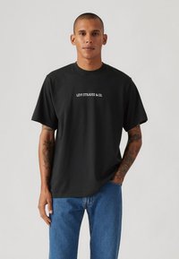Svart bomull T-skjorte med rund hals, korte ermer, og hvit brodert "LEVI STRAUSS & CO." logo på brystet. Avslappet passform.