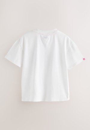 Witte katoenen T-shirt met korte mouwen, gezien van de achterkant, met een klein roze label op de rechtermouw en lichtroze stiksel bij de kraag.