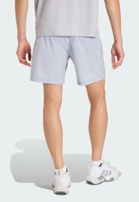 Lysegrå treningsshorts med jevn tekstur og reflekterende detaljer. Modellen kombinerer dem med hvite joggesko og enkel grå t-skjorte.