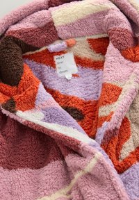 Fleece blanket with a patchwork design in shades of pink, purple, orange, and brown. Soft texture with a prominent label saying "NEXT time to dream."