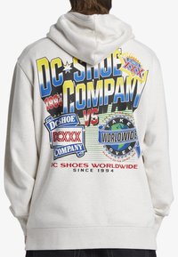 Jasnoszara bluza z kapturem z kolorowymi nadrukami graficznymi na plecach, w tym tekstem i logo, o luźnym kroju i kapturze ze ściągaczem.