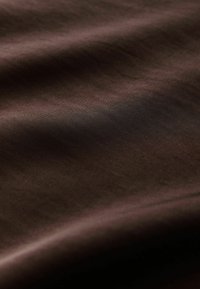 Tissu lisse de couleur brun foncé avec des plis subtils et une texture douce sous un éclairage doux.