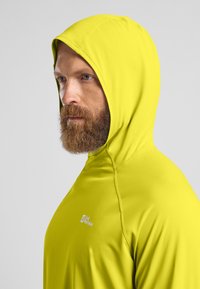 Maglietta a maniche lunghe con cappuccio di colore giallo brillante, realizzata in tessuto morbido, con una vestibilità aderente e un logo sulla spalla. Visibili dettagli delle cuciture.