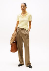 Stribet gul polo, beige høj talje bukser, strikket tan sweater over armen og sorte sko, med en brun tote taske.
