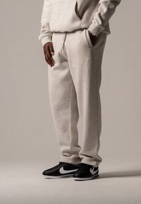 Helle graue Jogginghose mit weiter Passform, Kordelzugbund und Seitentaschen, kombiniert mit schwarzen Nike-Sneakern mit weißem Swoosh.