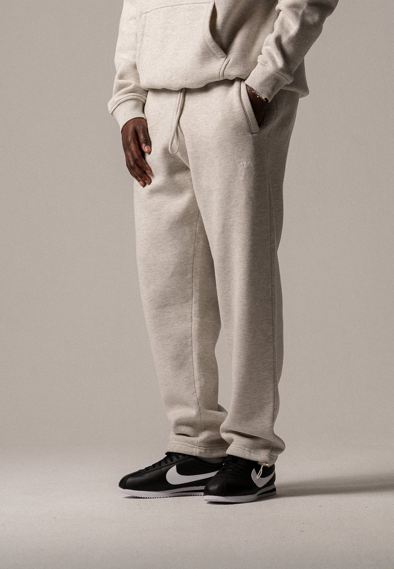 Helle graue Jogginghose mit weiter Passform, Kordelzugbund und Seitentaschen, kombiniert mit schwarzen Nike-Sneakern mit weißem Swoosh.