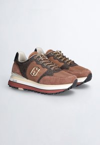 Sneaker marroni e neri con materiali in suede e mesh, dotati di un dettaglio logo, accenti a motivo e una suola bianca e rossa.