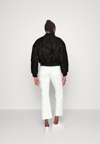 Zwarte doorgestikte bomberjack met glanzende afwerking, oversized pasvorm, geribbelde manchetten en zoom, gecombineerd met witte broek met rechte pijpen en sneakers.