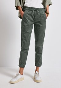 Gröna joggerbyxor i bomullsblandning med elastisk midja, dragsko, sidofickor och ribbade anklar, tillsammans med vita avslappnade sneakers.