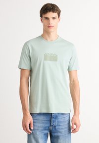 Pusiau žalia trumpomis rankovėmis marškinėliai, kurių priekyje subtilus tamsiai žalias "HUGO" logotipas. Pagaminti iš minkštos tekstūros medvilnės.