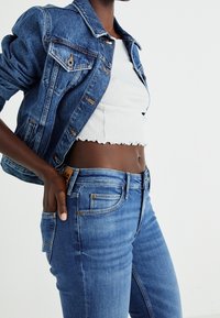 Denim takki keskisinisena vaskitootedega, kaasas valgest ribatopsist ja helesinistest sirgetest pükstest, millel on klassikalised taskud.