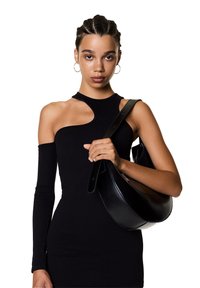 Robe noire côtelée avec un col asymétrique, associée à un sac à main en cuir noir incurvé avec une longue bandoulière.