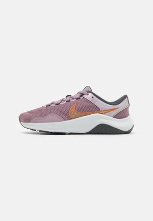 Zapatilla deportiva Nike en malla morada clara con un acabado texturizado, con acento del logo en naranja y media suela blanca con suela exterior negra.