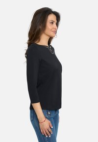 Top negro de manga tres cuartos con escote redondeado y costuras decorativas. Combinado con unos vaqueros azules, que presentan un corte relajado.