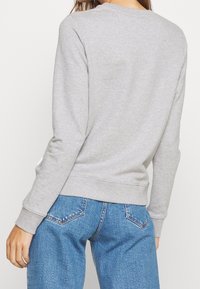 Grå sweatshirt med lange ærmer, ribbede manchetter og kant, lavet af blødt materiale. Synlig mærke på venstre side søm, stylet med blå jeans.